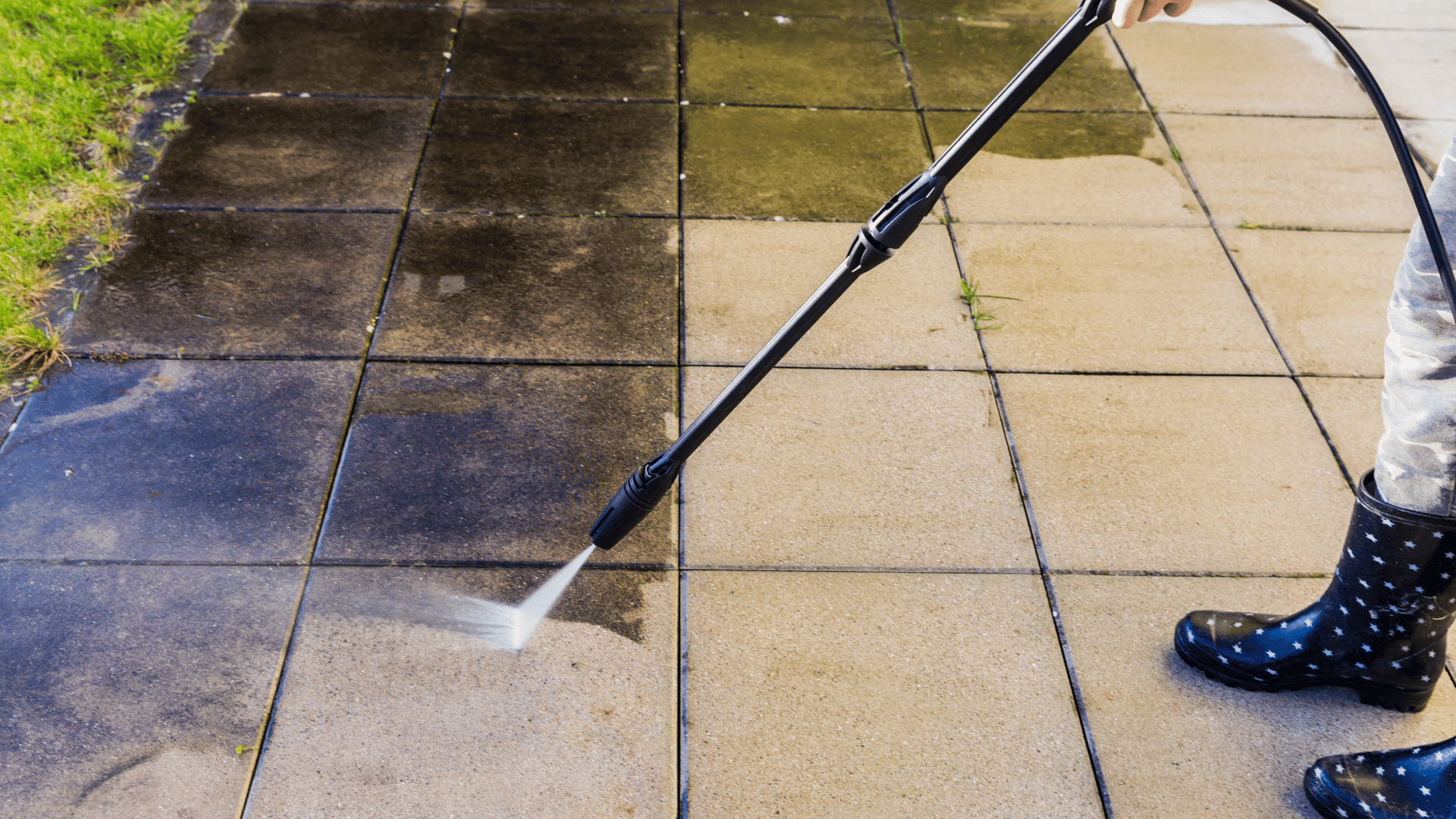 A person in rain boots is cleaning a sidewalk