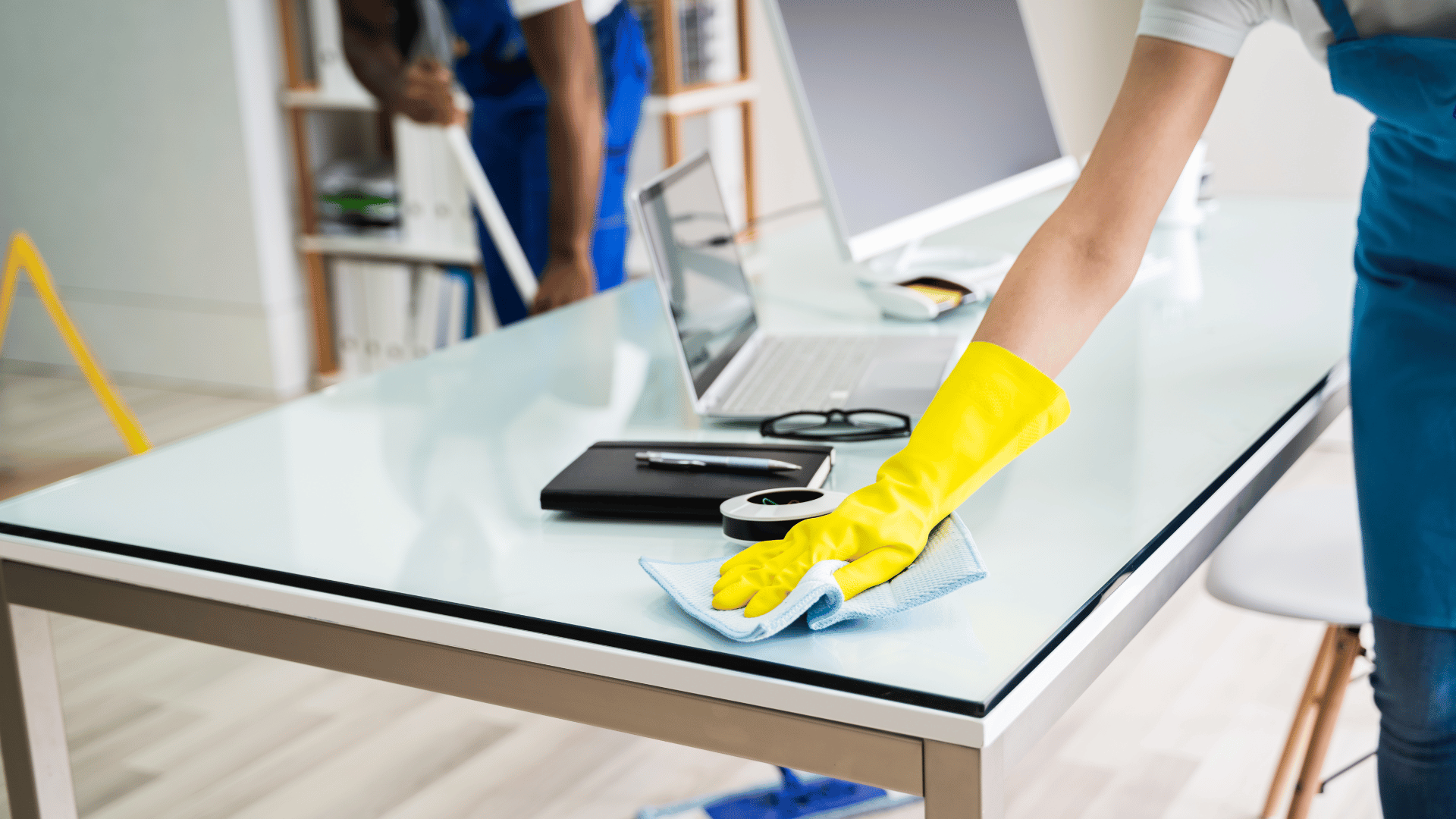 A person cleaning a desk with a yellow glove