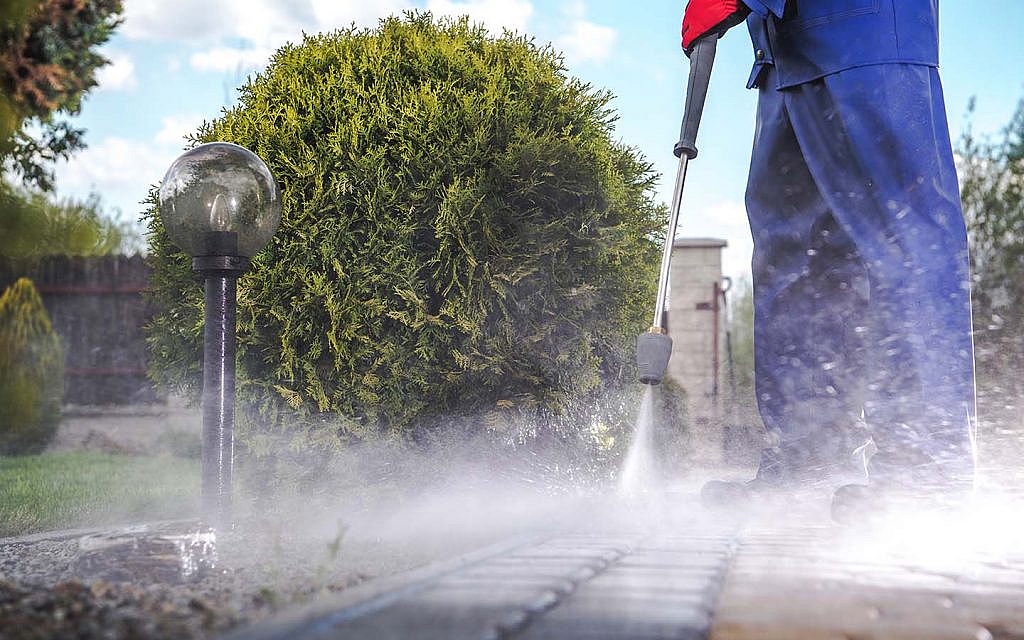 A man is using a pressure washer to clean a garden